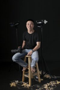 Photographer sitting in studio with camera gear, smiling and confident.