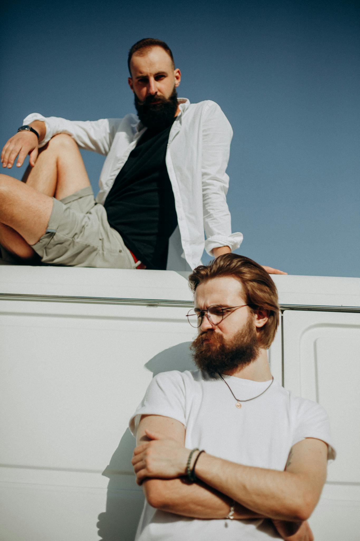 Two bearded men pose casually outdoors in daylight, exuding a relaxed vibe.